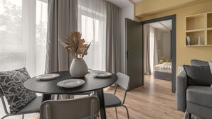 A modern living room with a round dining table, two chairs, a vase with dried plants, and a grey sofa. - Apartio Rooms Zabrze (Zabrze)