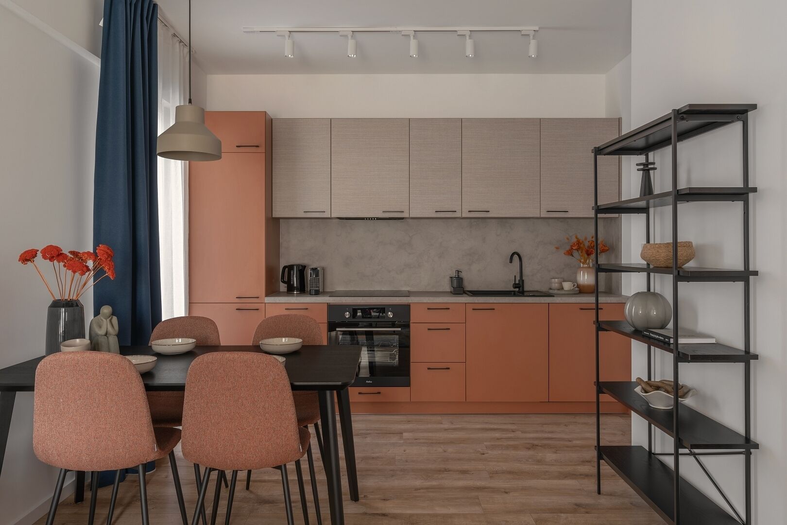 Ett modernt kök med en matplats, med ett svart matbord, rosa stolar, en kaffemaskin och en inbyggd ugn.