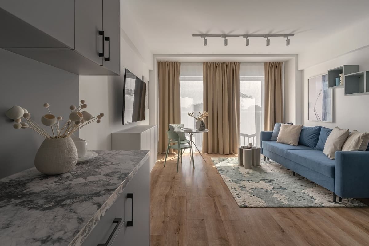 Een moderne woonkamer met een blauwe bank, een eethoek met een tafel en stoelen, en een keuken met een marmeren aanrecht.