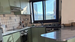 A modern kitchen with green cabinets, a large window, and a view of a cityscape. - Penthouse with Rooftop & Mountain View - Between Sea, Nature & Relaxation (Poli Chrysochous)