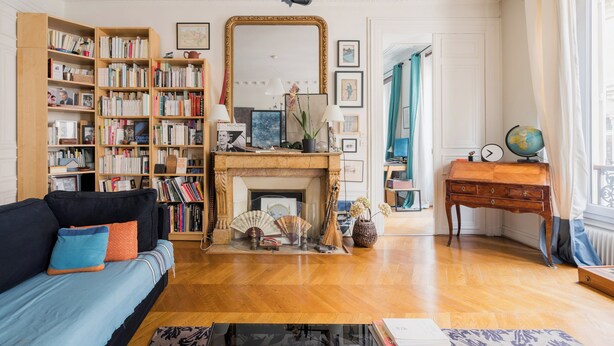 Una sala de estar bien iluminada con chimenea, estanterías, un sofá y una pequeña mesa con un globo terráqueo.