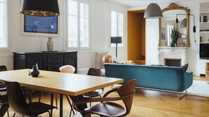A spacious living room with a wooden dining table, chairs, a teal sofa, and a fireplace.