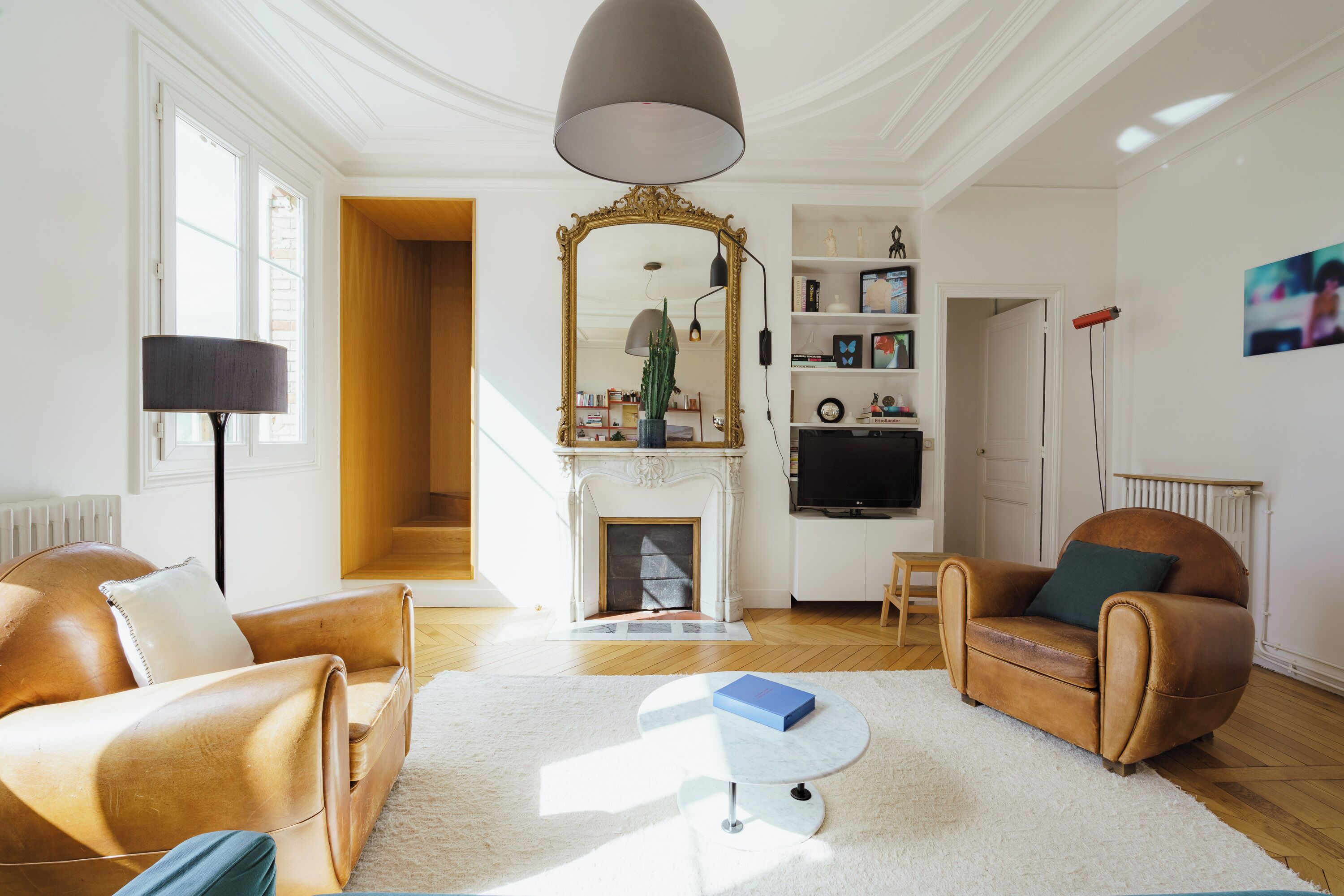 A living room with a fireplace, two leather sofas, a round coffee table, and a large mirror.