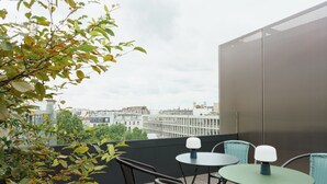 A balcony with two tables and chairs, overlooking a cityscape.