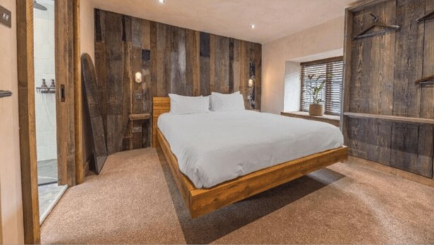 Ein Schlafzimmer mit einem hölzernen Bettgestell, einem großen Fenster mit Jalousien und einem Holzschrank.