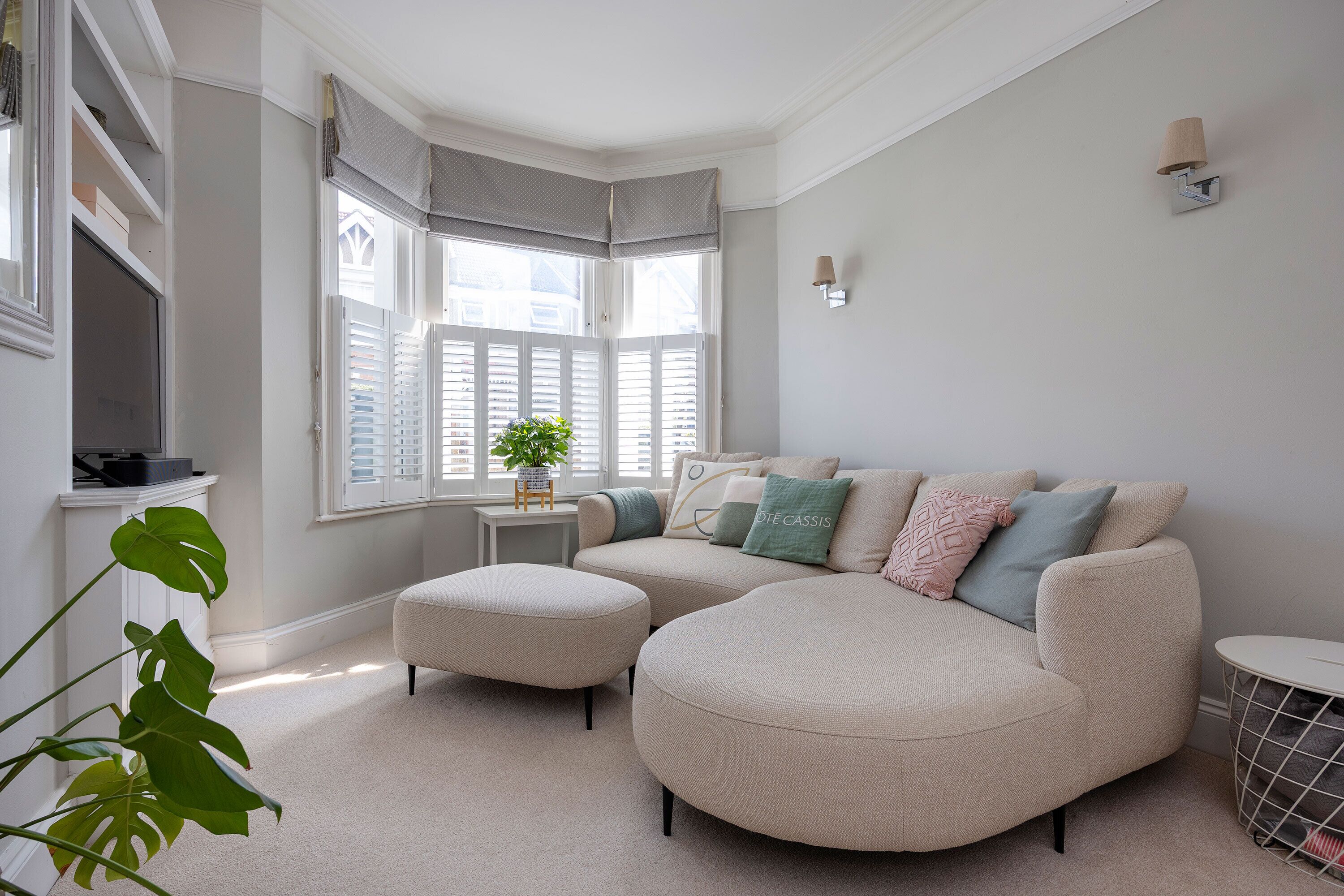 A modern living room with a curved sofa, a small side table, and a window with shutters.