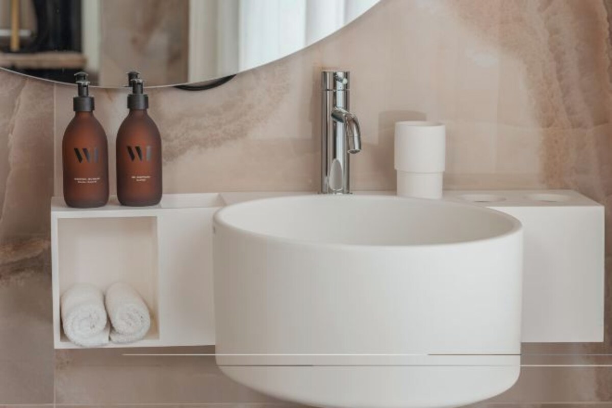 A bathroom with a large white sink, two brown bottles, a faucet, and a towel rack with towels.