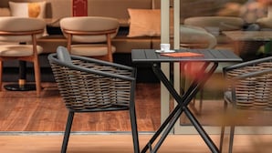 Un interno moderno con un divisorio in vetro, sedie in vimini, un tavolo nero e un divano con cuscini.