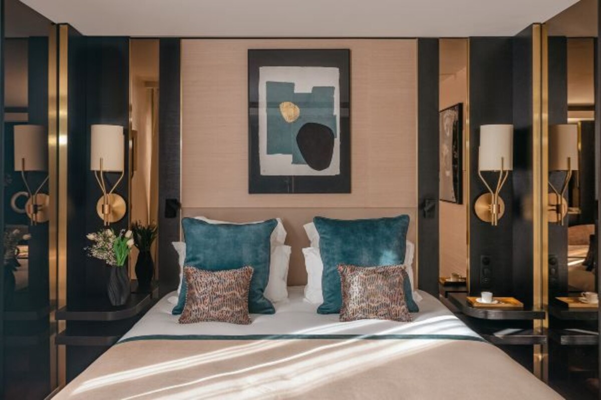 A hotel room with a large bed, two bedside tables, a wall-mounted artwork, and a vase with flowers.