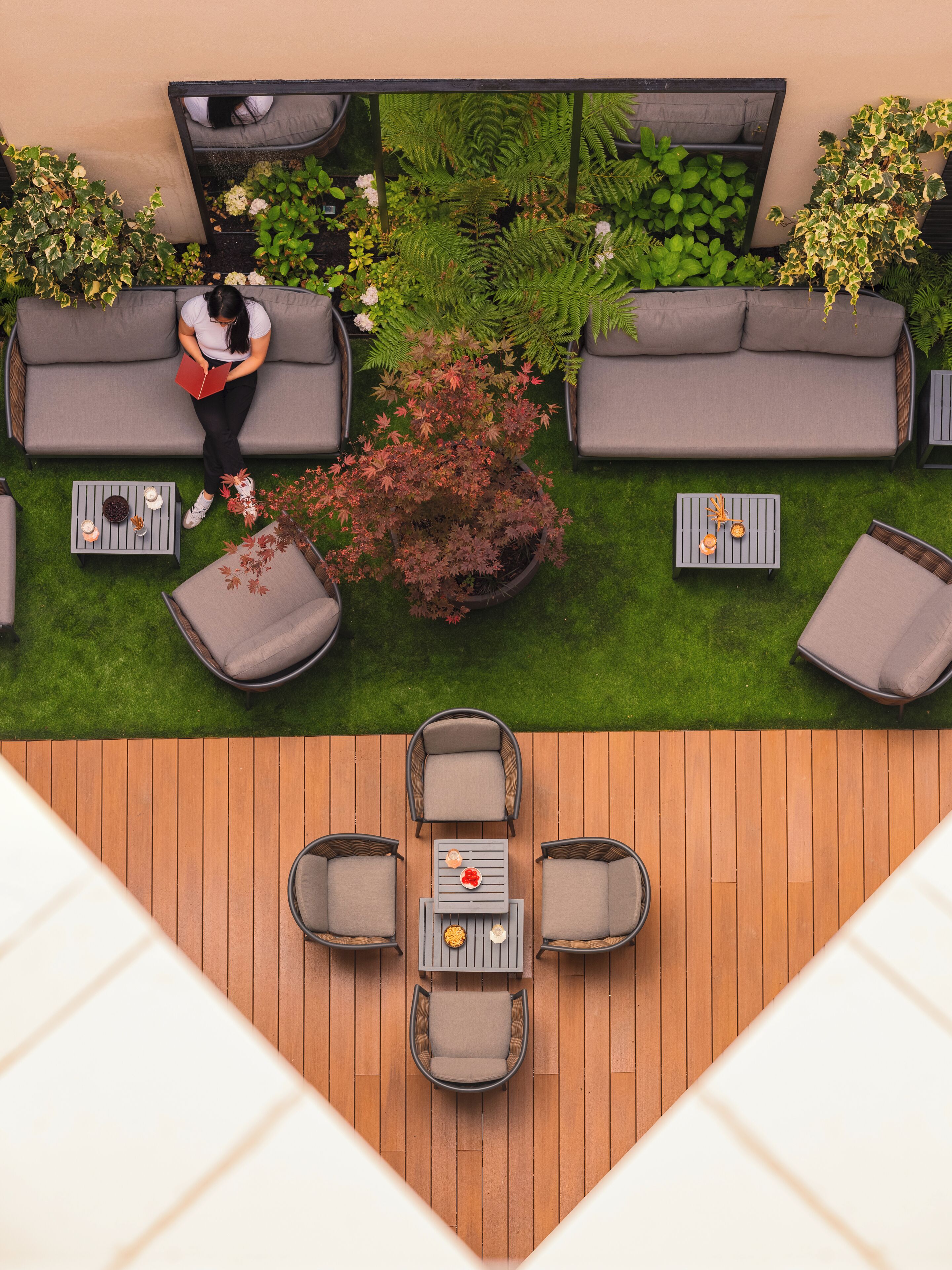 An outdoor seating area with a wooden deck, grey sofas, and a central table with chairs.