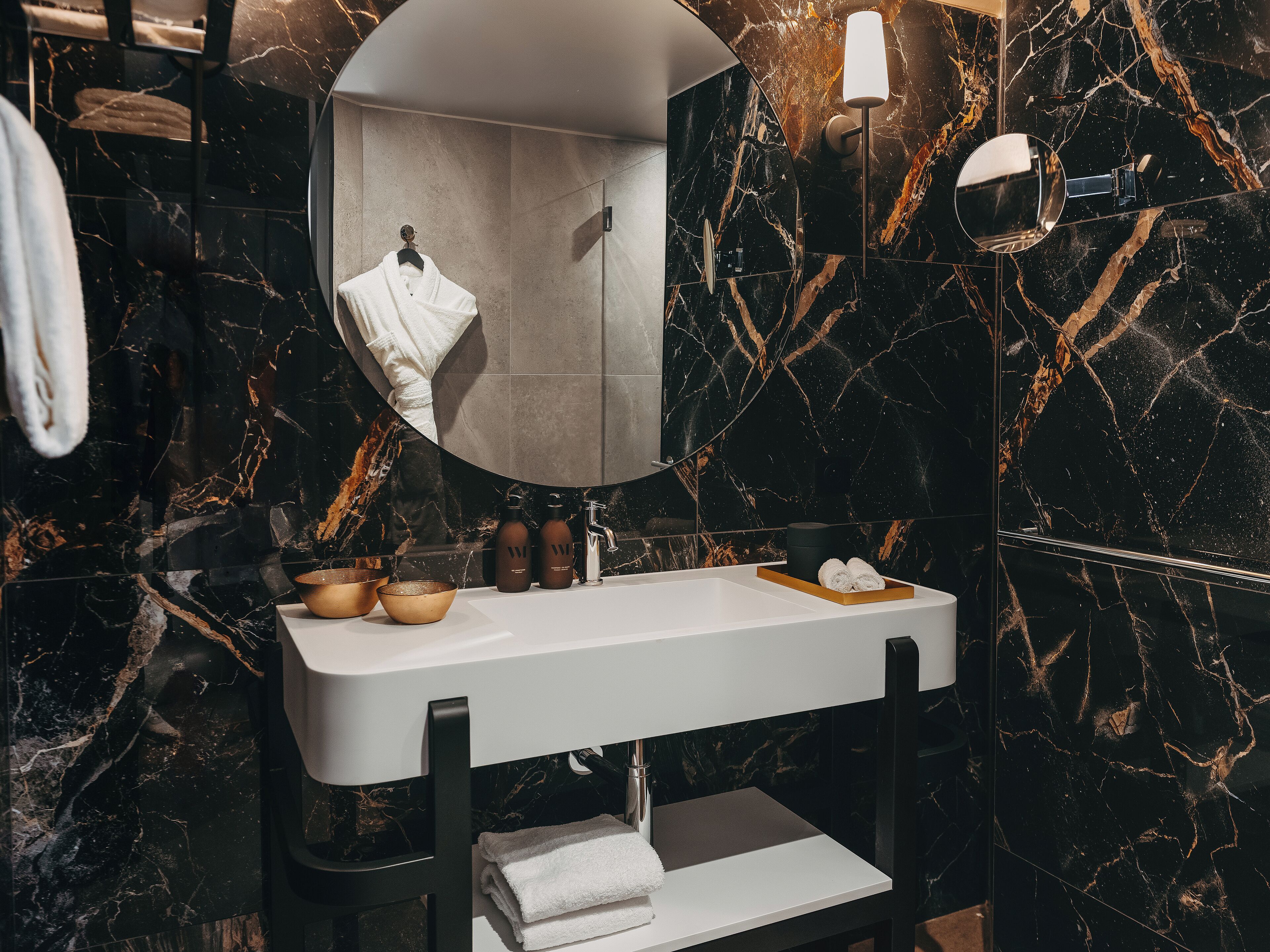 Un baño moderno con un lavabo de mármol negro, un espejo y un perchero.