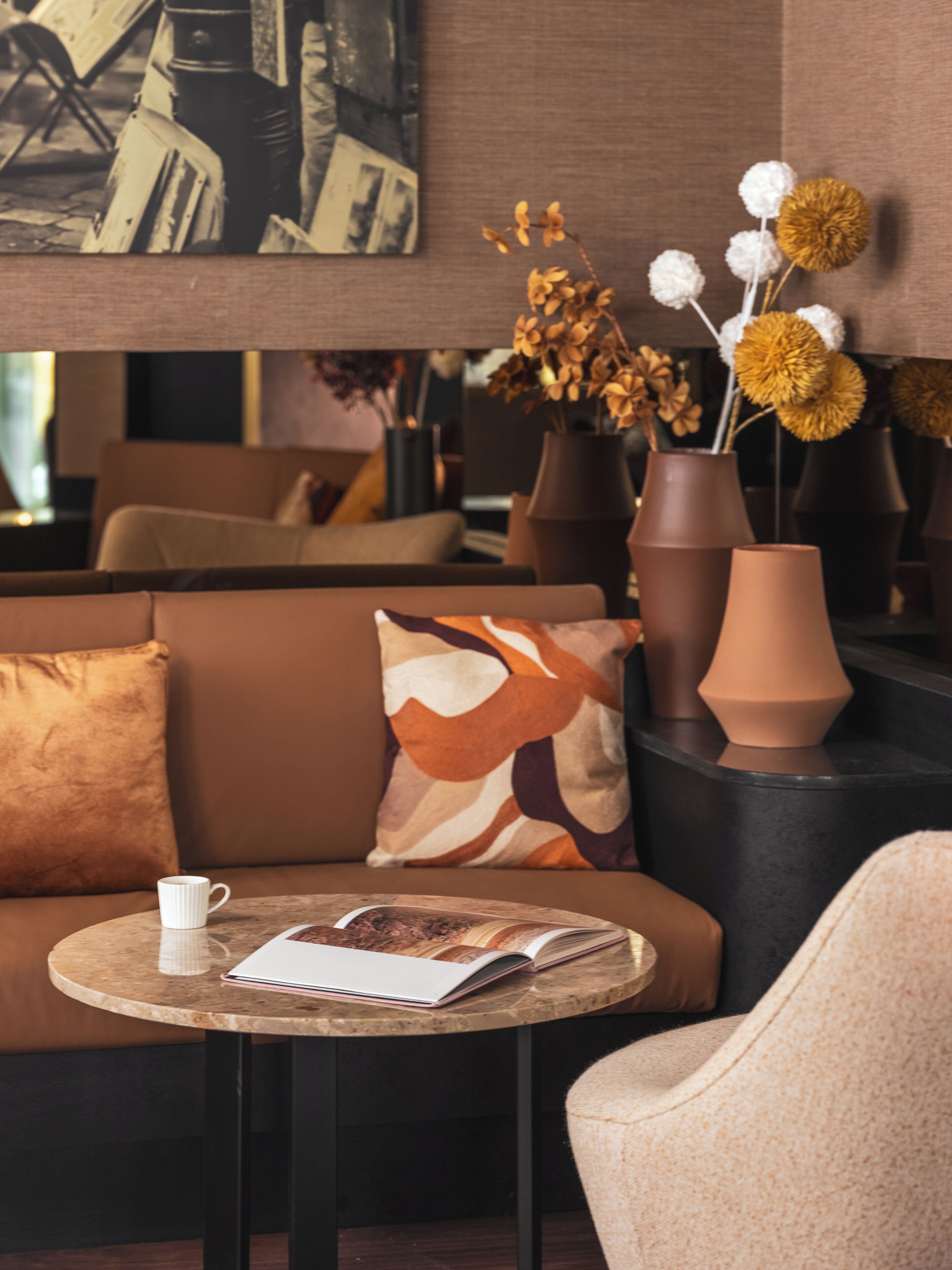 A modern lounge area with a sofa, a round table with a magazine, and decorative vases with dried flowers.
