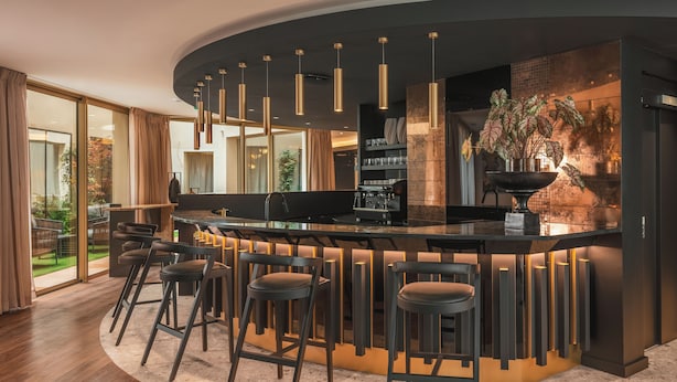 Una cucina moderna con isola a forma di ferro di cavallo, sgabelli da bar, illuminazione a sospensione e vista sul giardino esterno.