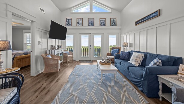 A spacious living room with a large blue sofa, a flat-screen TV, and a dining area with wicker furniture. - Waterfront Paradise in N. Topsail: Ocean/Canal Views, Fishing, Steps from Beach (North Topsail Beach)