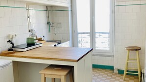 A kitchen with a checkered floor, a wooden table, a stool, and a window with a view. - Bright, quiet apartment near Panier, Vieux-Port, Joliette (Marseille)