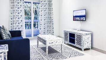 A living room with a blue sofa, patterned curtains, a white cabinet with a TV on the wall, and a patterned rug.