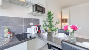 Cocina moderna con microondas, hervidor y varios alimentos sobre la encimera. Hay una mesa de comedor con platos y un jarrón de flores.