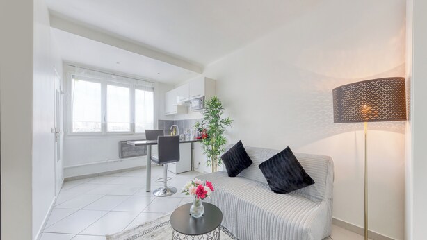 Una sala de estar moderna con un sofá, una mesita de centro con flores, una lámpara de pie y vistas a la cocina.