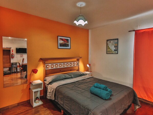 Un dormitorio con una cama de madera, una mesita de noche, una lámpara roja, un espejo y dos cuadros en la pared.