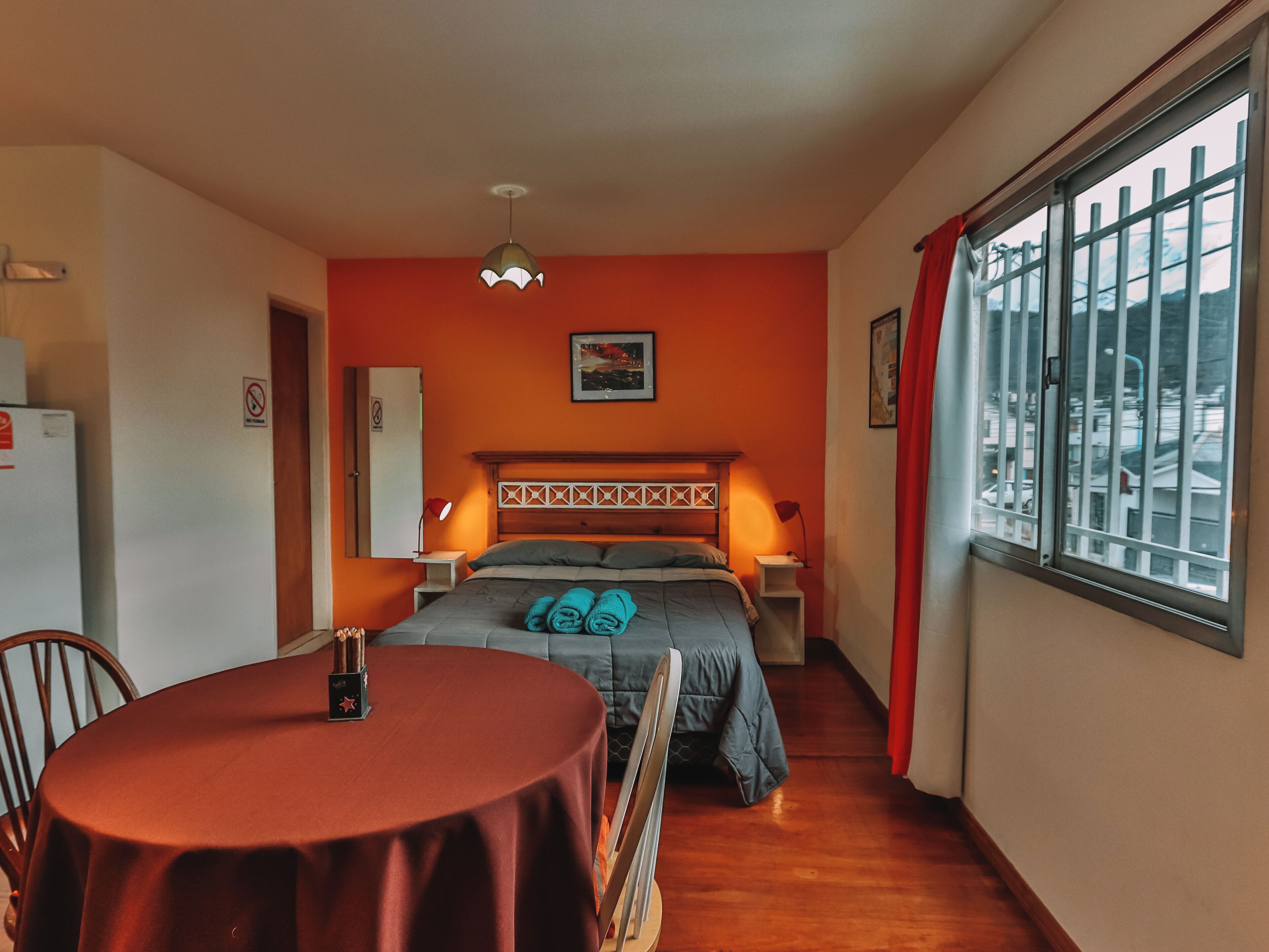 Ein kleines Hotelzimmer mit Bett, einem kleinen Tisch, einem Sessel, einem Fenster mit Blick und einer Deckenleuchte.