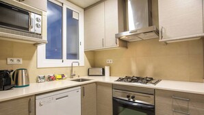 Une cuisine compacte équipée d’un lave-vaisselle, d’une cuisinière, d’un four à micro-ondes et d’une fenêtre avec des panneaux en verre dépoli.