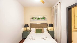 Une chambre d’hôtel avec un lit, deux tables de chevet, un ventilateur de plafond, un tableau et une porte.