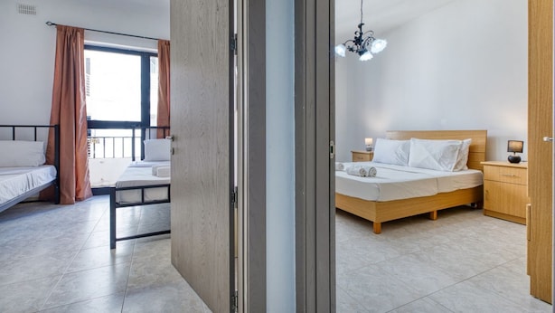 Ein modernes Hotelzimmer mit einem hölzernen Bett, einem separaten Schlafbereich mit einer Couch, einem kleinen Nachttisch mit einer Lampe und Blick durch eine Schiebetür.
