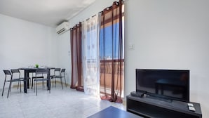 Ein modernes Wohnzimmer mit Fernseher, einem Esstisch mit Stühlen und einem Balkon mit Vorhängen.