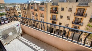 Ein Balkon mit Blick auf mehrstöckige Gebäude, einer großen Klimaanlage und einem Metallgeländer.