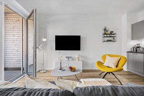 A modern living room with a sofa, a yellow armchair, a round coffee table, and a flat-screen TV mounted on the wall. - Modern apartment with terrace, partial sea view and private parking in Travemünd (Lübeck)