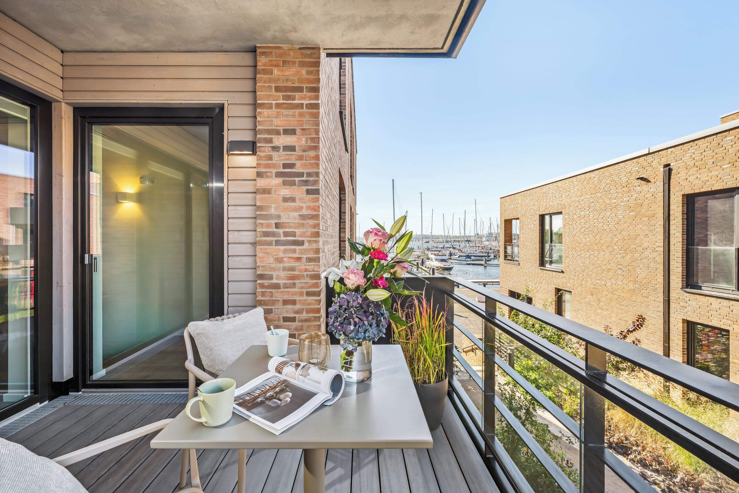 Een balkon met een tafel voor twee, een bloevas en uitzicht op een jachthaven.