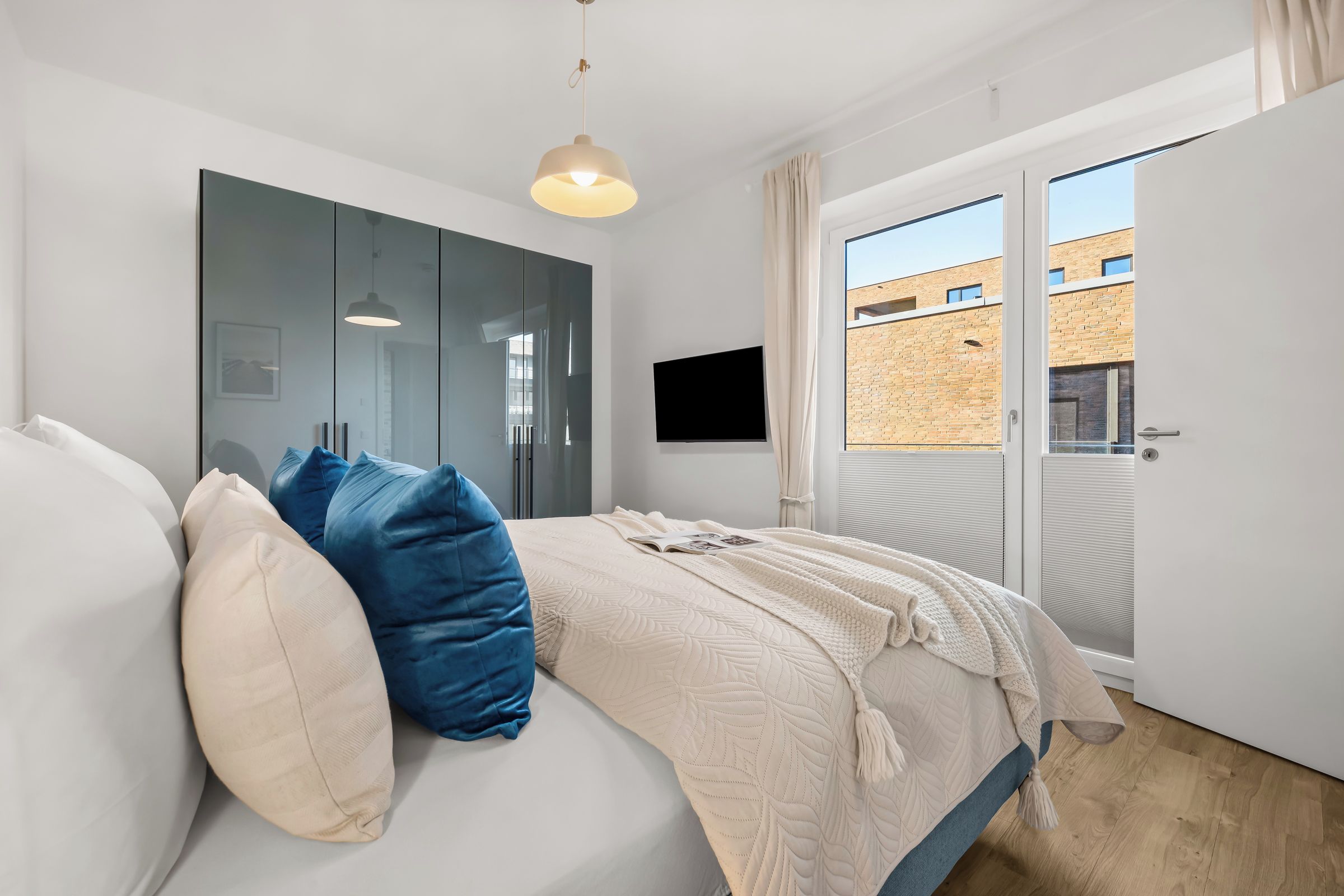Ein Schlafzimmer mit Bett, Kleiderschrank, Fernseher und Blick ins Freie.