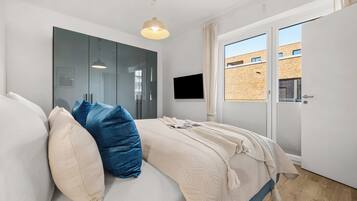 Ein Schlafzimmer mit Bett, Kleiderschrank, Fernseher und Blick ins Freie.