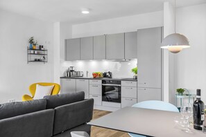 A modern kitchen with grey cabinets, a built-in oven, and a dining area with a grey sofa and a table. - Modern apartment with terrace, partial sea view and private parking in Travemünd (Lübeck)