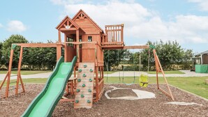A wooden play structure with a slide, climbing wall, and swings. - The Cabin (Malton)