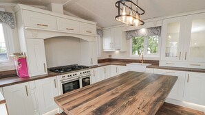 A modern kitchen with white cabinetry, a large wooden island, a gas stove, and a pendant light. - The Cabin (Malton)