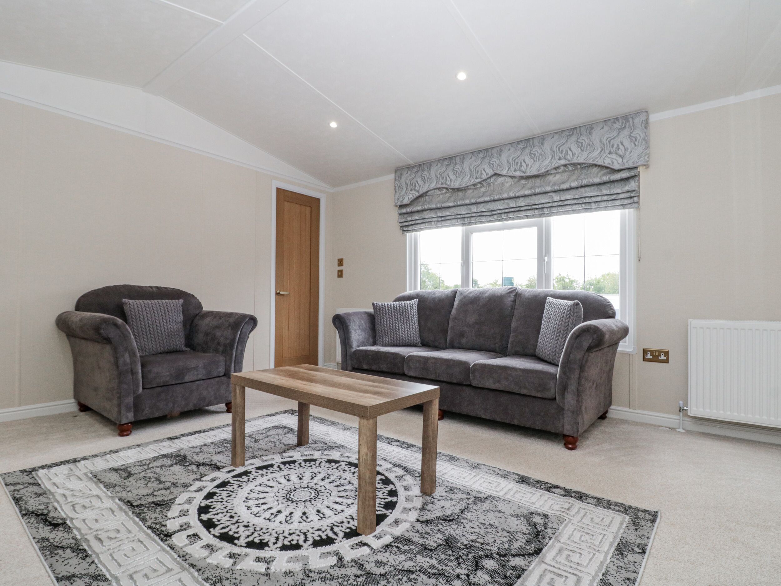 Ein Wohnzimmer mit zwei grauen Sofas, einem Holztisch und einem gemusterten Teppich.
