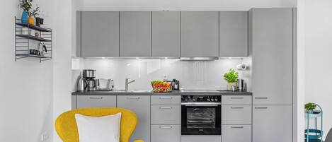 A modern kitchen with grey cabinets, a built-in oven, and a coffee machine.