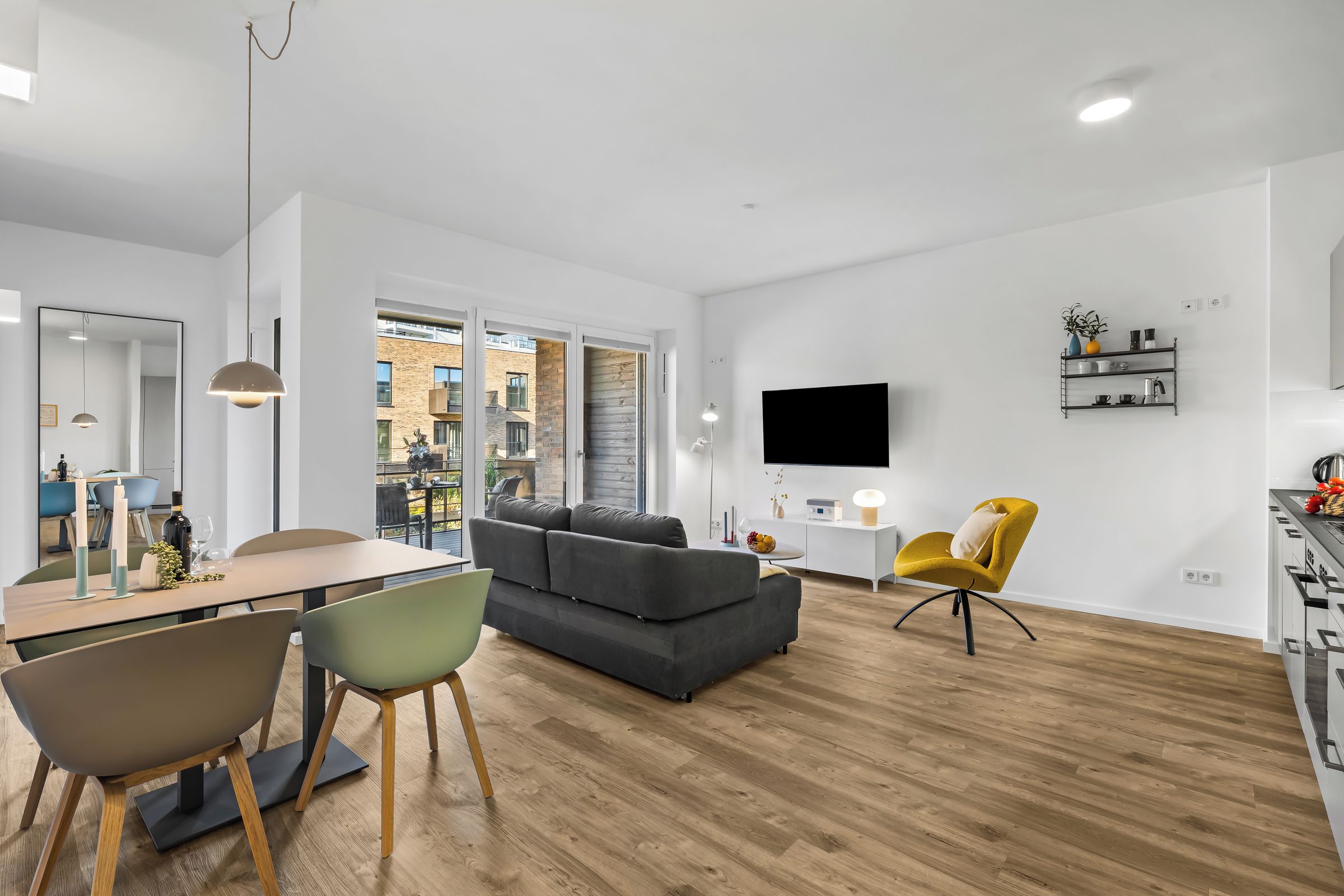 Ein modernes Wohnzimmer mit einem grauen Sofa, einer Essecke mit Tisch und Stühlen, einem gelben Sessel und einem an der Wand befestigten Fernseher.