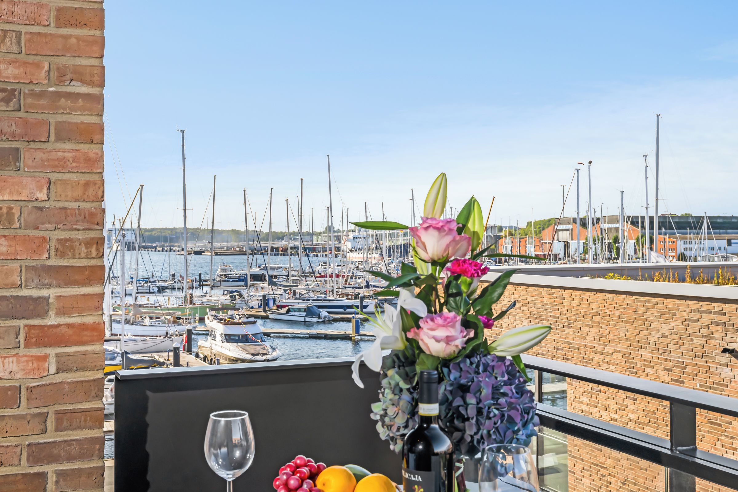 A balcony with a view of a marina, a glass of wine, and a bouquet of flowers.