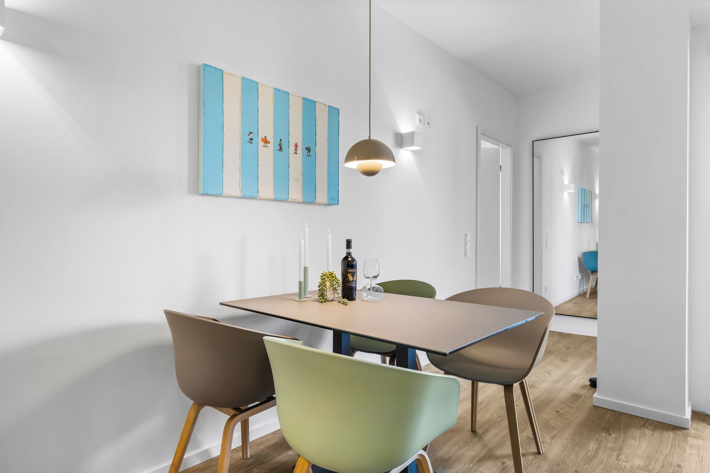 Ein moderner Essbereich mit einem rechteckigen Tisch, vier Stühlen, einer Pendelleuchte und einem an der Wand befestigten Kunstwerk.
