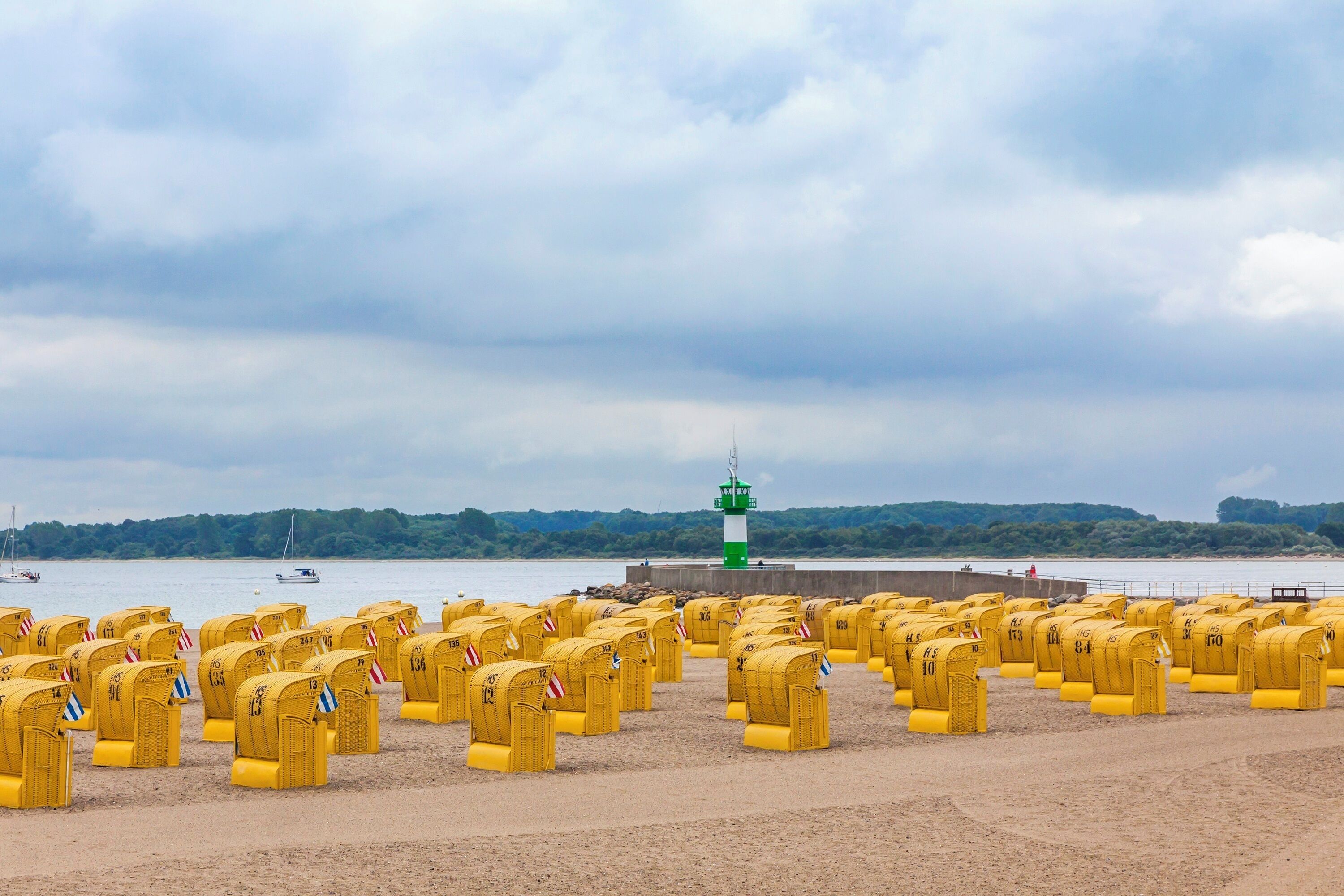 A beach with yellow mailboxes arranged in rows, a lighthouse in the background, and a calm sea.