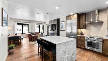 A modern kitchen with a marble island, stainless steel appliances, and wooden cabinetry.