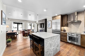 A modern kitchen with a marble island, stainless steel appliances, and wooden cabinetry. - Slope! There It Is! | Exclusive Tamarack Perks (Tamarack)