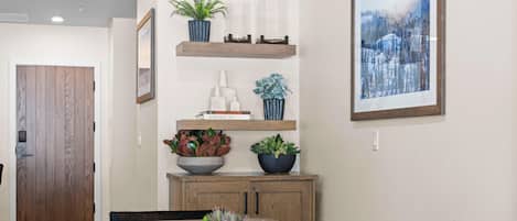 A dining area with a wooden table, chairs, a bowl of plants, and a framed picture on the wall.