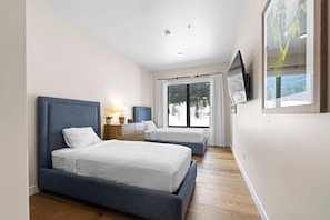A modern hotel room with two beds, a large window with a view, a flat-screen TV, and a wooden floor. - Slope! There It Is! | Exclusive Tamarack Perks (Tamarack)