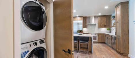 Een wasruimte met gestapelde wasmachines en een moderne keuken met houten kastjes en een centraal eiland.