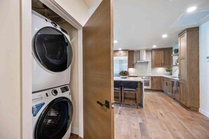 Un área de lavandería con lavadoras apiladas y una cocina moderna con armarios de madera y una isla central.