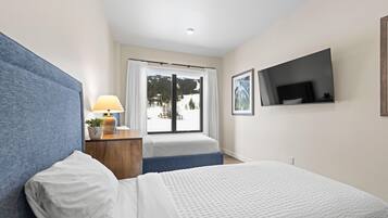 Una habitación de hotel con una cama, un escritorio con lámpara, un televisor en la pared y una ventana con vistas a un paisaje nevado.