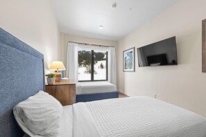 Una habitación de hotel con una cama, un escritorio con lámpara, un televisor en la pared y una ventana con vistas a un paisaje nevado.